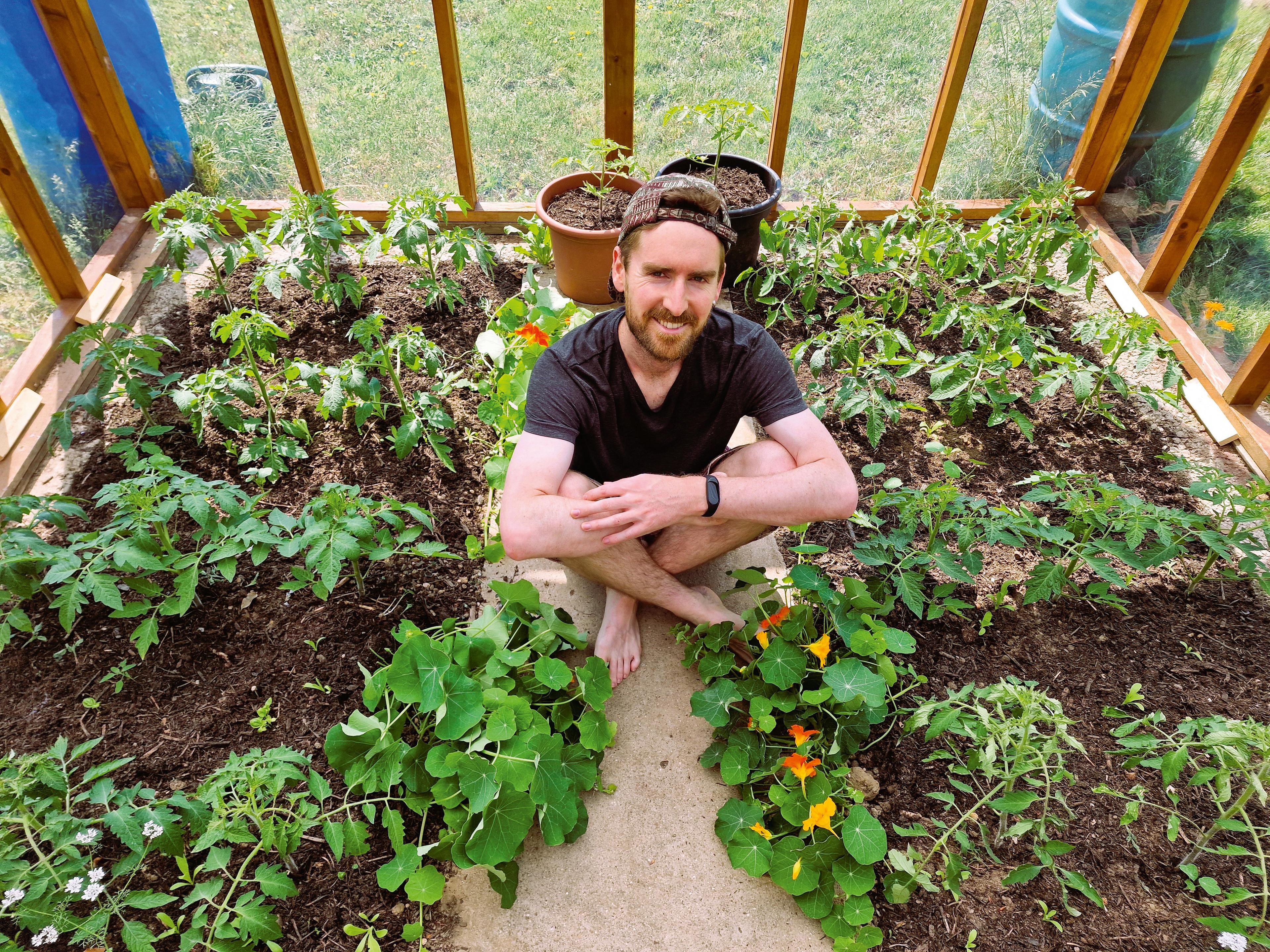 David Spencer sits on the ground in his greenhouse