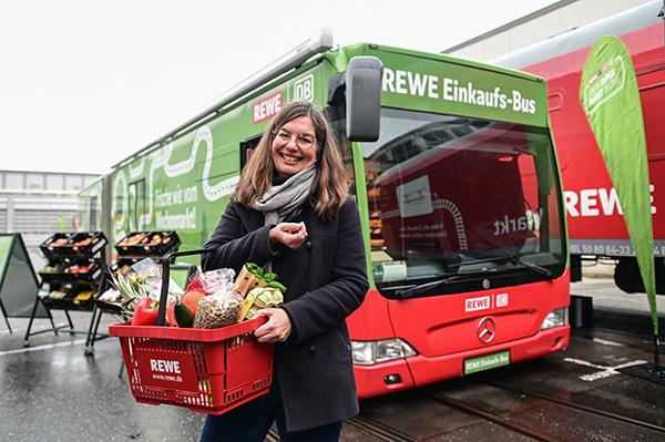 A woman with products in a basket and behind her is a train from REWE