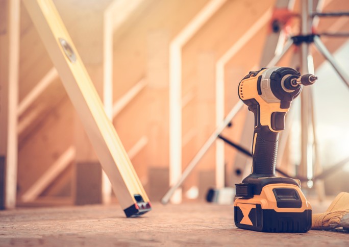 A close-up of a cordless drill. In the background a wooden construction.